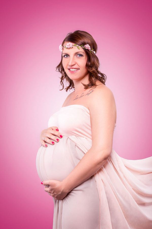 Fotograf Schwarzwald Babybauch Frau in Kleid und Blumenband im Haar vor Rosa Hintergrund