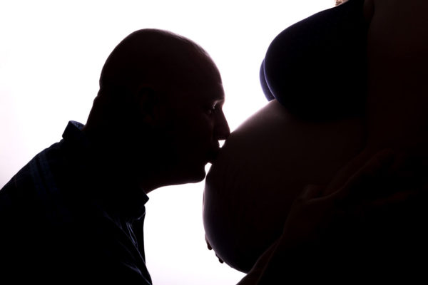 Fotograf Schwarzwald Babybauch Mann küsst den Bauch seiner Frau vor weißem Hintergrund