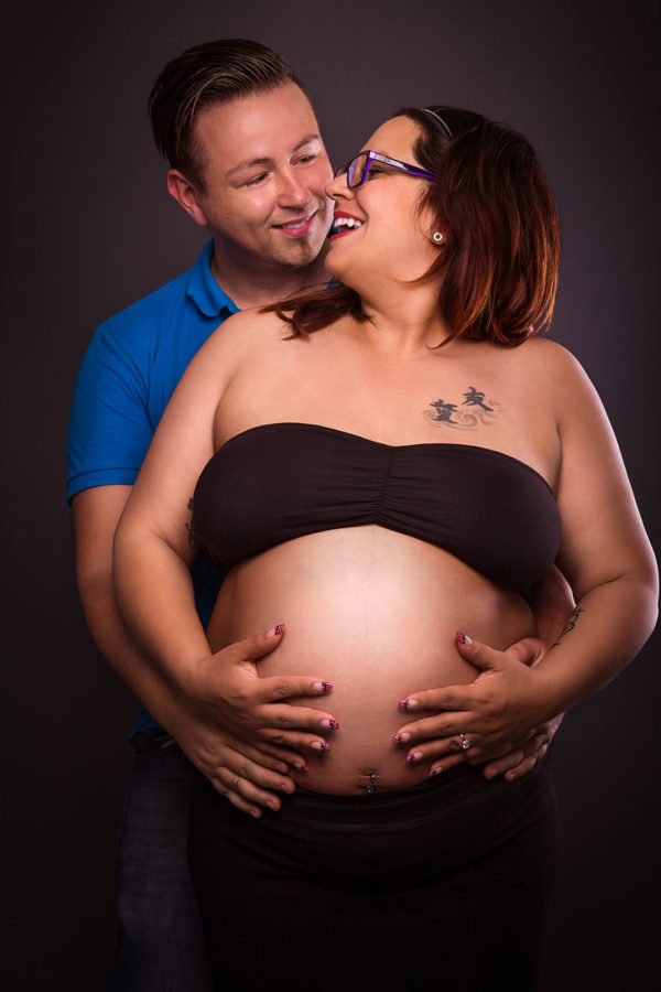 Fotograf Schwarzwald Babybauch Mann hält seine Frau hinten und schauen sich verliebt an
