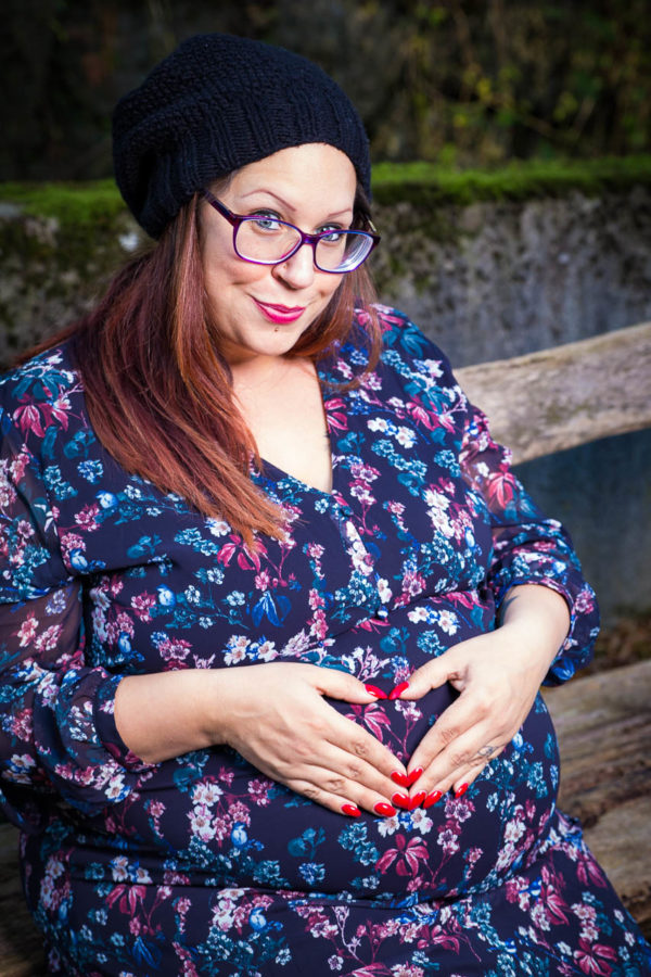 Fotograf Schwarzwald Babybauch Frau mit Brille und Mütze formen ein Herz auf dem Babybauch