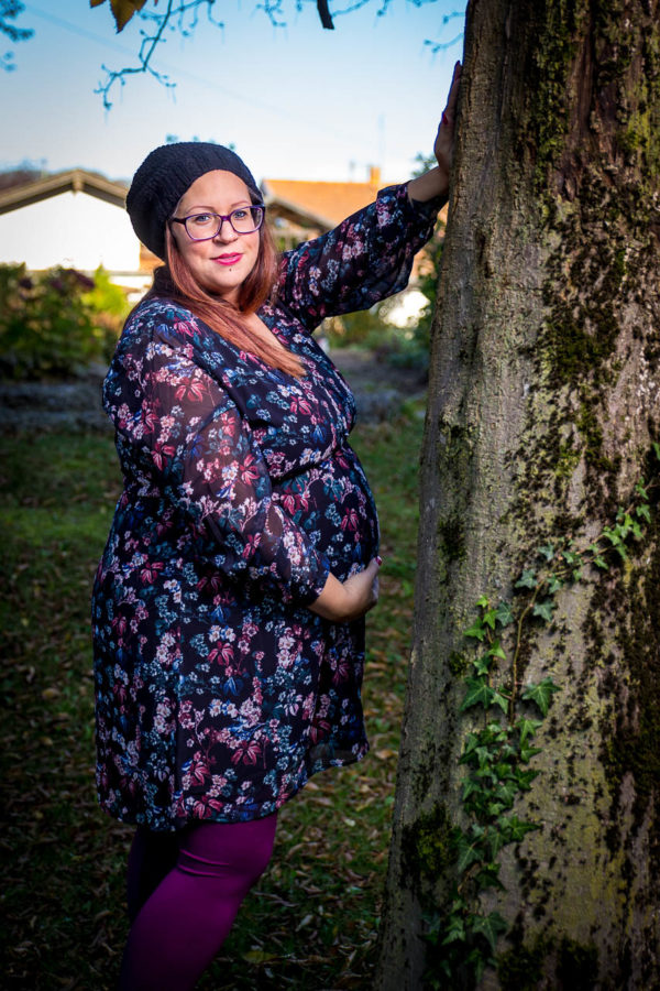 Fotograf Schwarzwald Babybauch Frau mit Brille und Mütze posiert an einem Baum