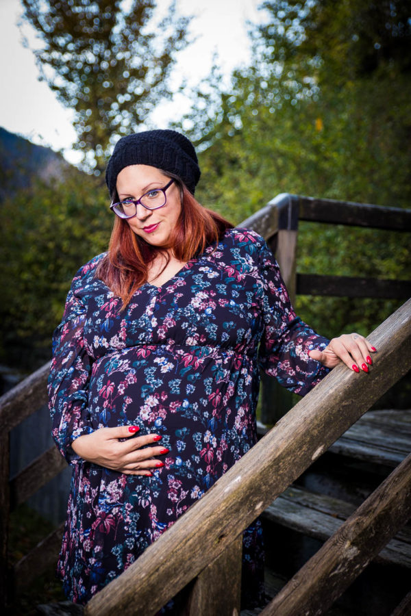 Fotograf Schwarzwald Babybauch Frau mit Brille und Mütze hält ihren Babybauch auf einer kleinen Holztreppe